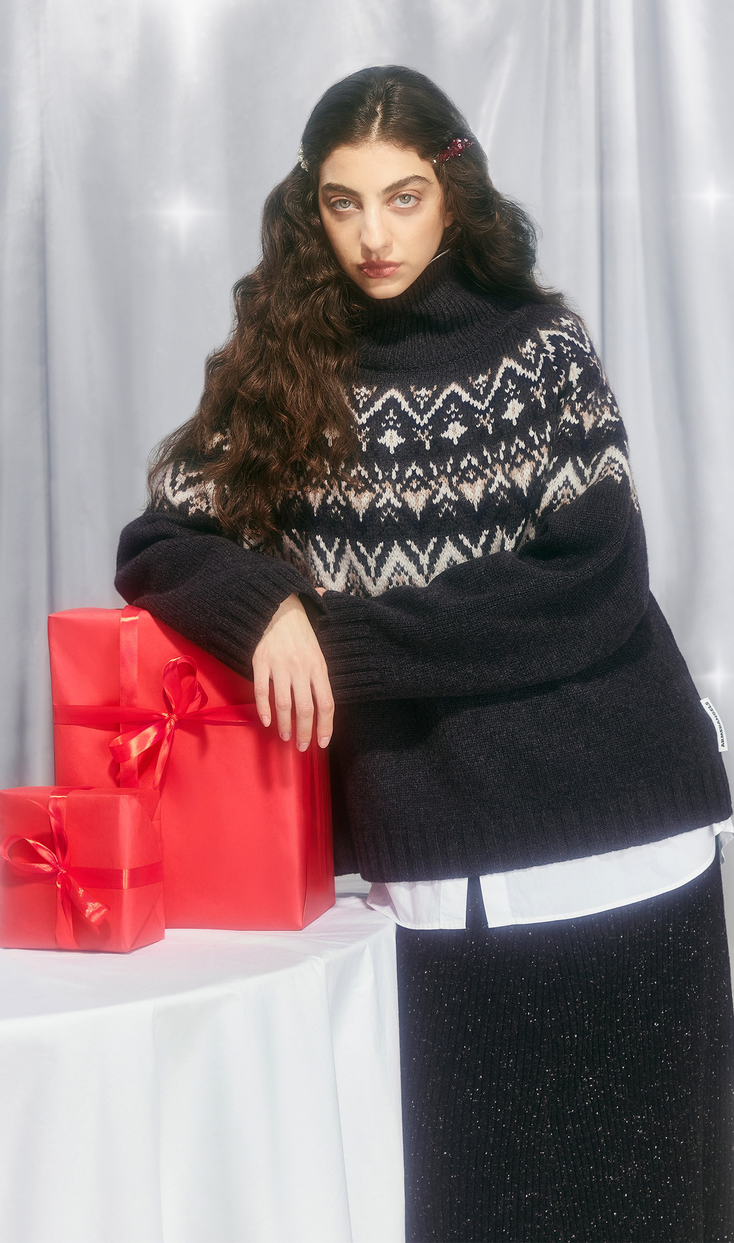 Eine Person in winterlichem Strickpullover lehnt an einem Tisch mit drei roten, festlich verpackten Geschenken.