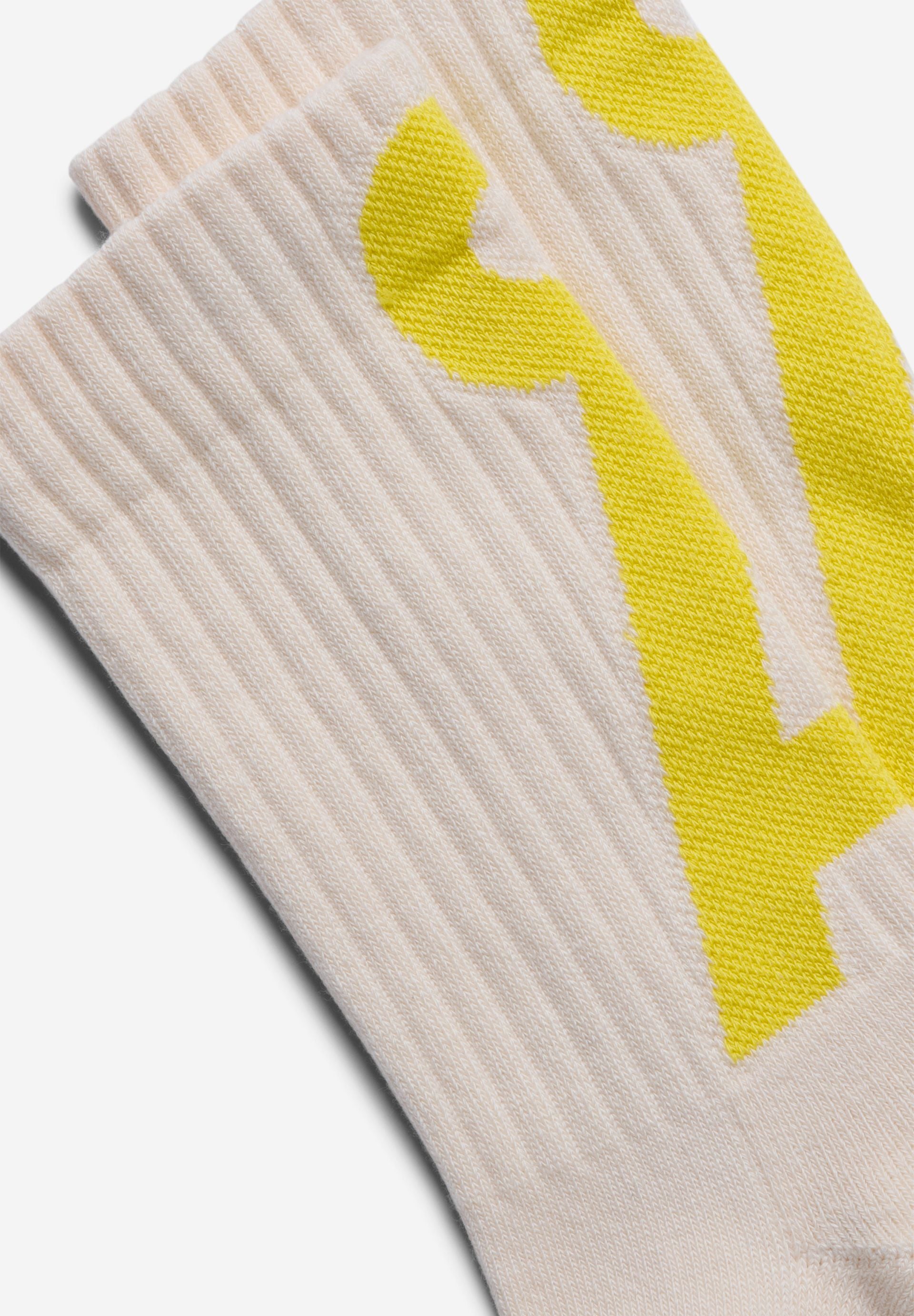 SAAMUS SHORT Socken in der Farbe pure-armedangels yellow mit gelbem Å-Logo vor hellem Hintergrund.
