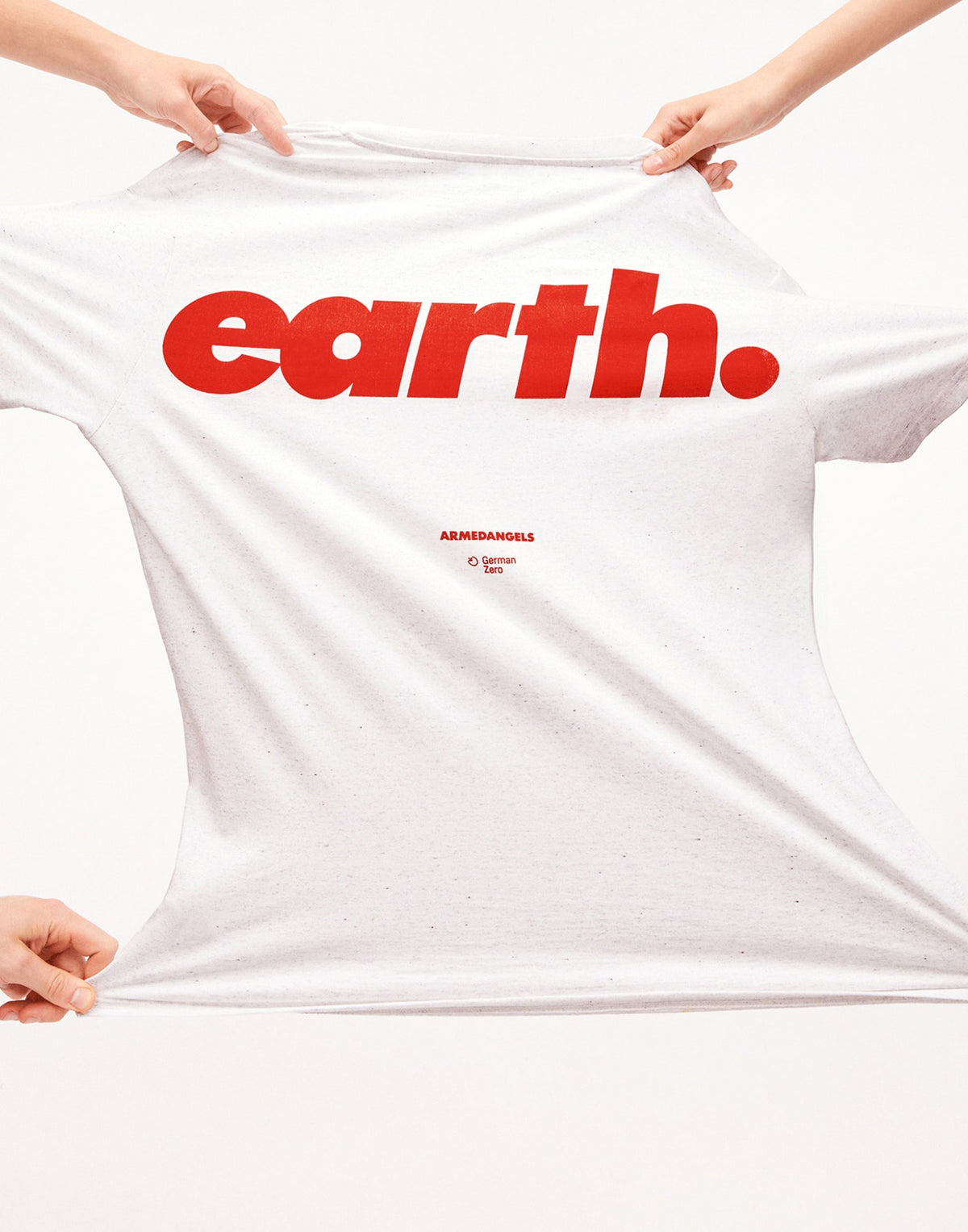 Nahaufnahme eines weißen T-Shirts mit großem roten Schriftzug ‚earth.‘ und kleinem Armedangels-Logo darunter; das Shirt wird seitlich gespannt gehalten.