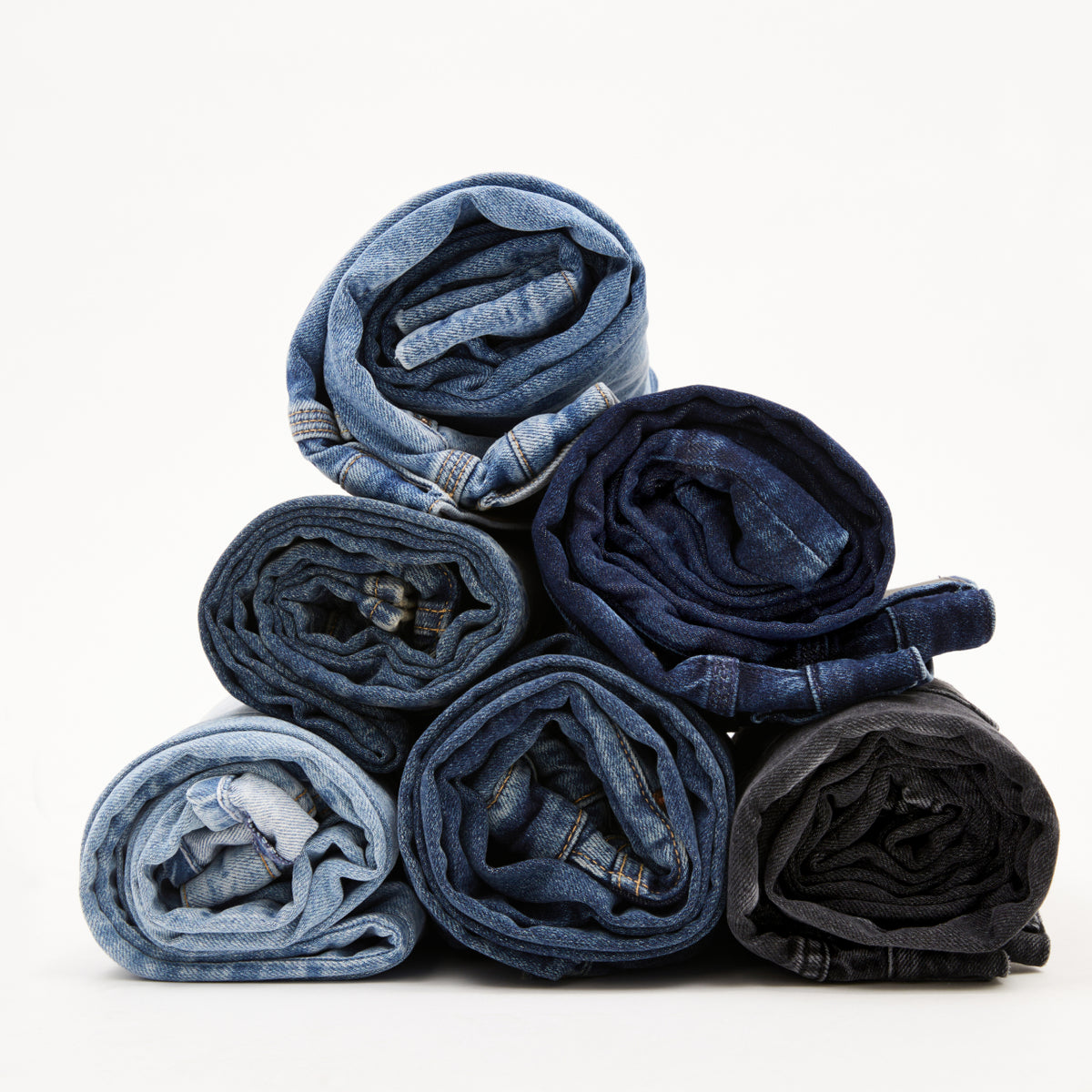 Sechs zusammengerollte Jeans in verschiedenen Blautönen und Schwarz, pyramidenförmig gestapelt.