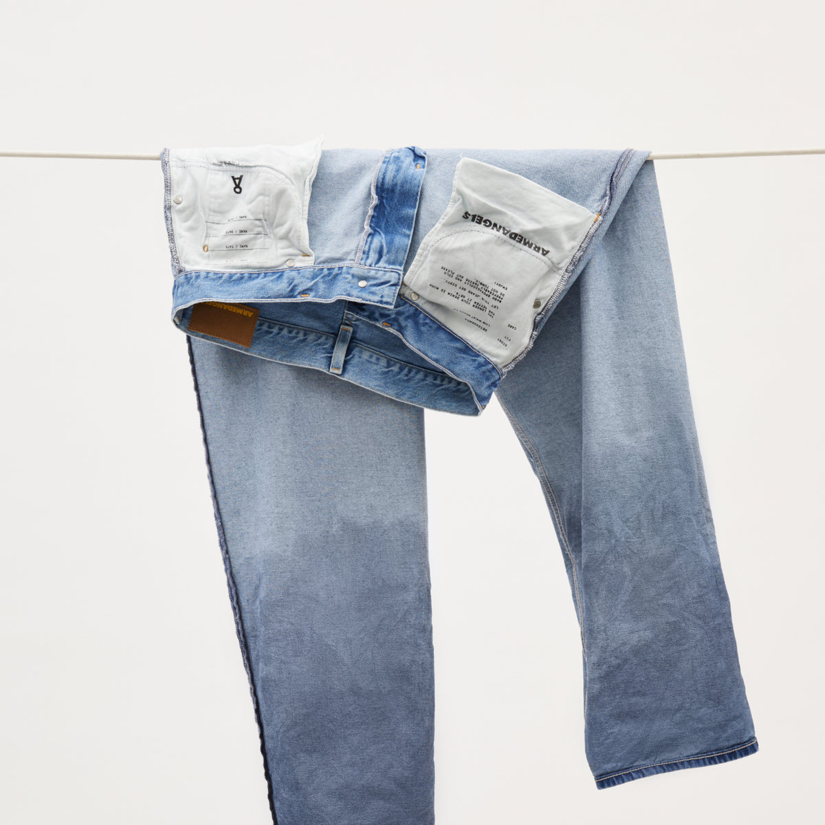 Jeans hängt auf links gedreht über einer Leine, Taschen zeigen Armedangels-Label und Produktionsdetails.